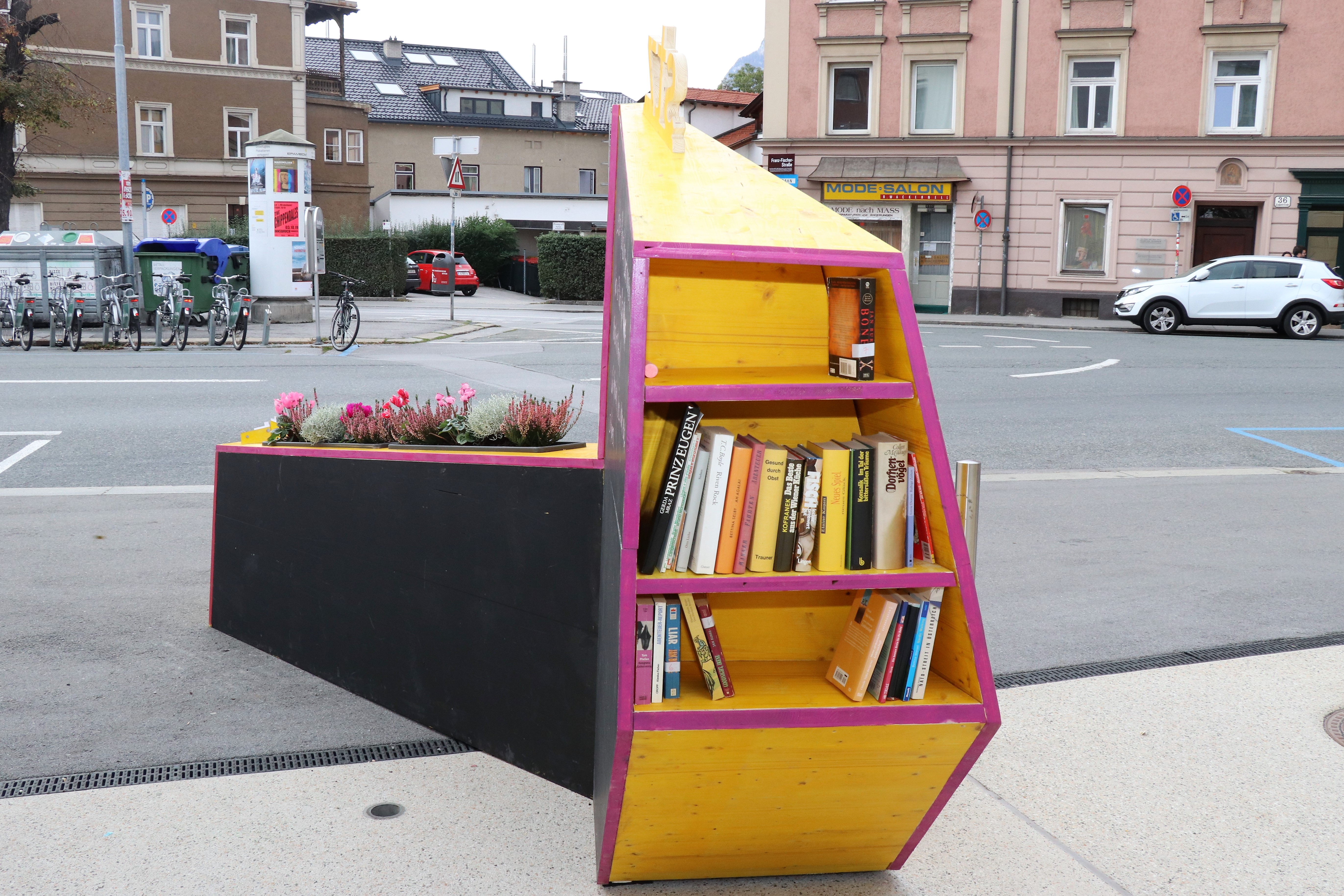 Kreativ, bunt und unübersehbar – so präsentiert sich seit 4. Oktober das temporäre, öffentliche Möbelstück vor dem Stadtteilzentrum Wilten in der Leopoldstraße 33a. Die Idee für das hölzerne Bauwerk entstand im Rahmen eines Beteiligungsprozesses bereits im Dezember 2017. Damals kamen NachbarInnen, ein Kreativteam aus Wilten und VertreterInnen des Stadtteilzentrums zusammen, um über die Gestaltung des Innenhofes zu beratschlagen. Die nun realisierte Konstruktion enthält die gewünschten Elemente, bestehend aus Beschriftung, Informations- und Plakatflächen, einem Buchtauschregal, Sitzgelegenheiten und kann mit Blumentöpfen ausgestattet werden. Bei der Einweihung kamen viele Beteiligte und UnterstützerInnen zusammen, unter ihnen auch Gemeinderätin Janine Bex, Geschäftsführer Hubert Innerebner (Innsbrucker Sozialen Dienste, ISD), Stadtteilkoordinatorin Florence Fritz sowie das Kreativteam rund um Charly Walter und zahlreiche AnrainerInnen. Bis Juni 2021 lädt das öffentliche Möbelstück vor dem Stadtteilzentrum Wilten zum Verweilen und Verwenden ein. AA